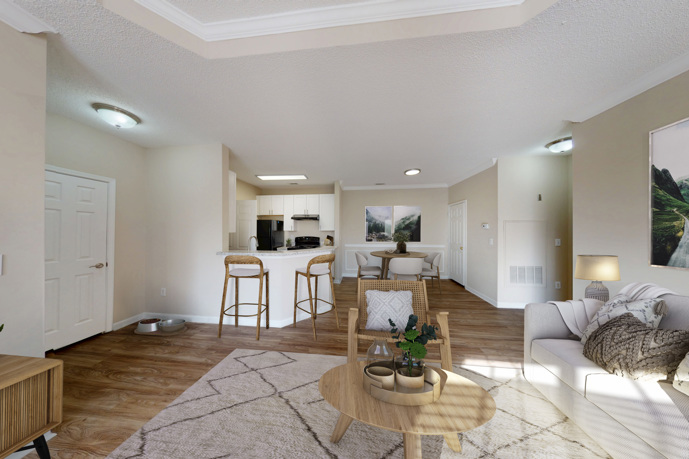 Neutral colored apartment living room with a white sofa in front of two grey ottomans and a dining area and small kitchen in the back